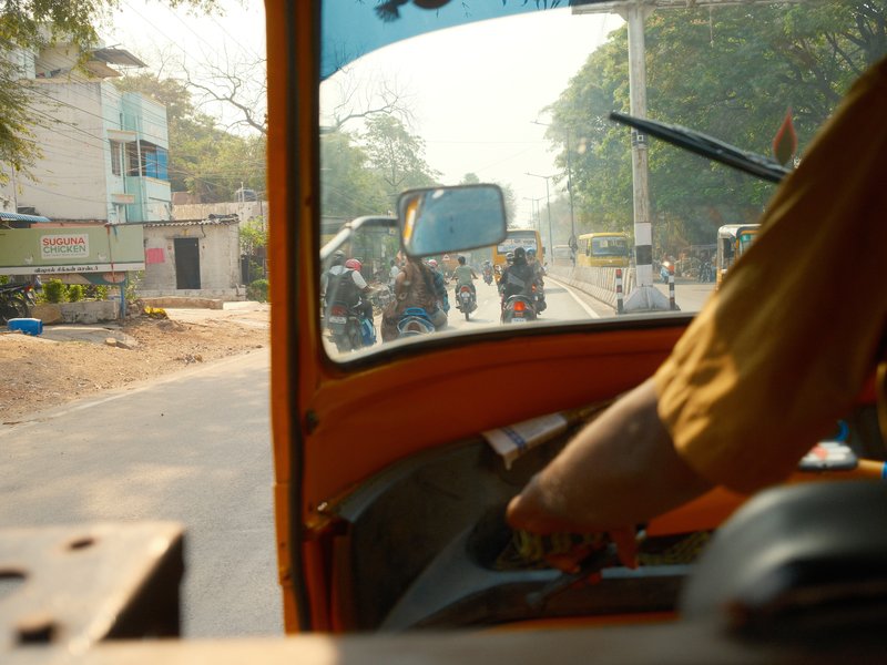 View from inside an auto rickshaw on a busy street with vehicles and buildings in the background.