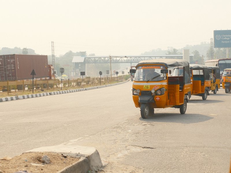 Three yellow auto rickshaws driving on a wide road with a hazy background.