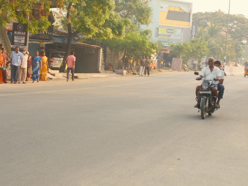 A street scene with a motorcycle and pedestrians in a warm, urban setting during the day.
