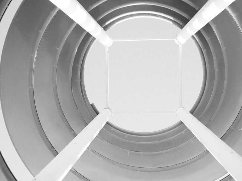 View looking up from inside a cylindrical structure with white walls and a square opening at the top.