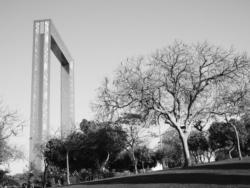A tall modern structure stands beside a leafless tree in a park setting under clear skies.