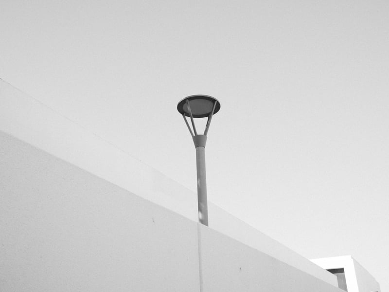 A minimalist street lamp against a clear sky, partially obscured by a white wall.