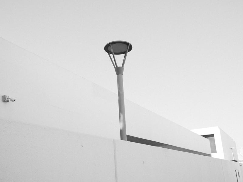 A minimalist urban scene featuring a tall street lamp against a stark white wall.