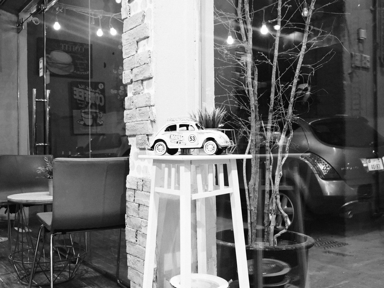 A vintage toy car on a white stool in a cafe, with blurred background elements and soft lighting.