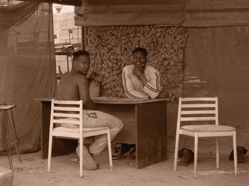 Two men seated at a table in a makeshift shelter, engaged in conversation.