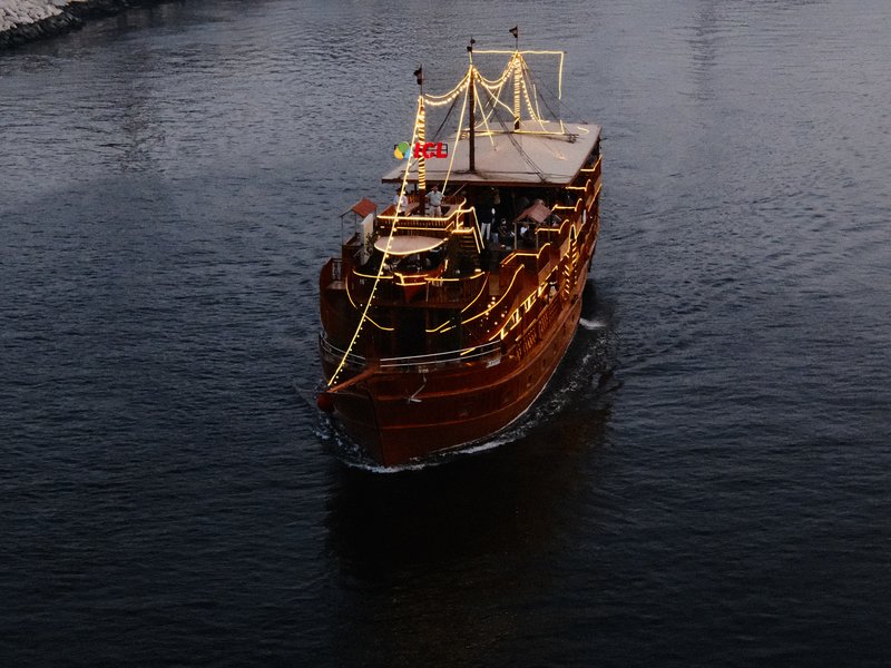 A wooden boat adorned with lights sailing on dark water, surrounded by a serene atmosphere.