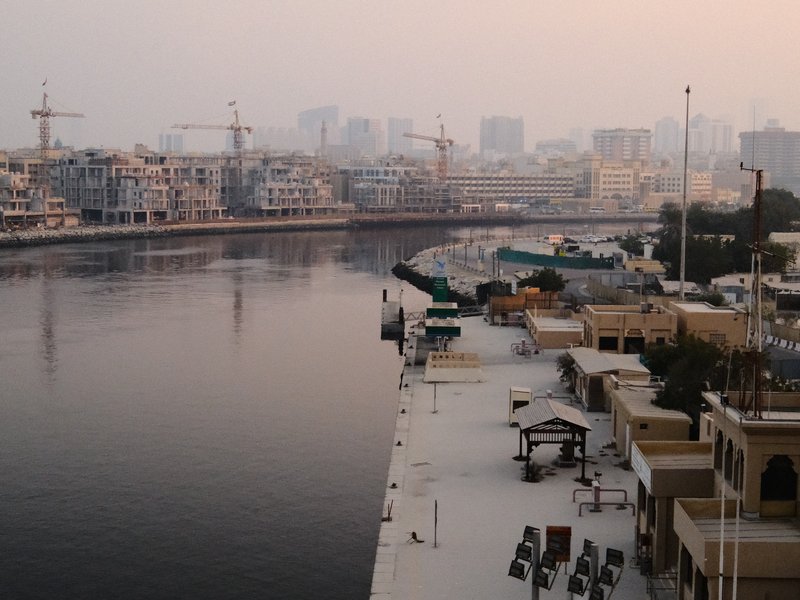 View of a river with buildings and cranes in the background during dusk.