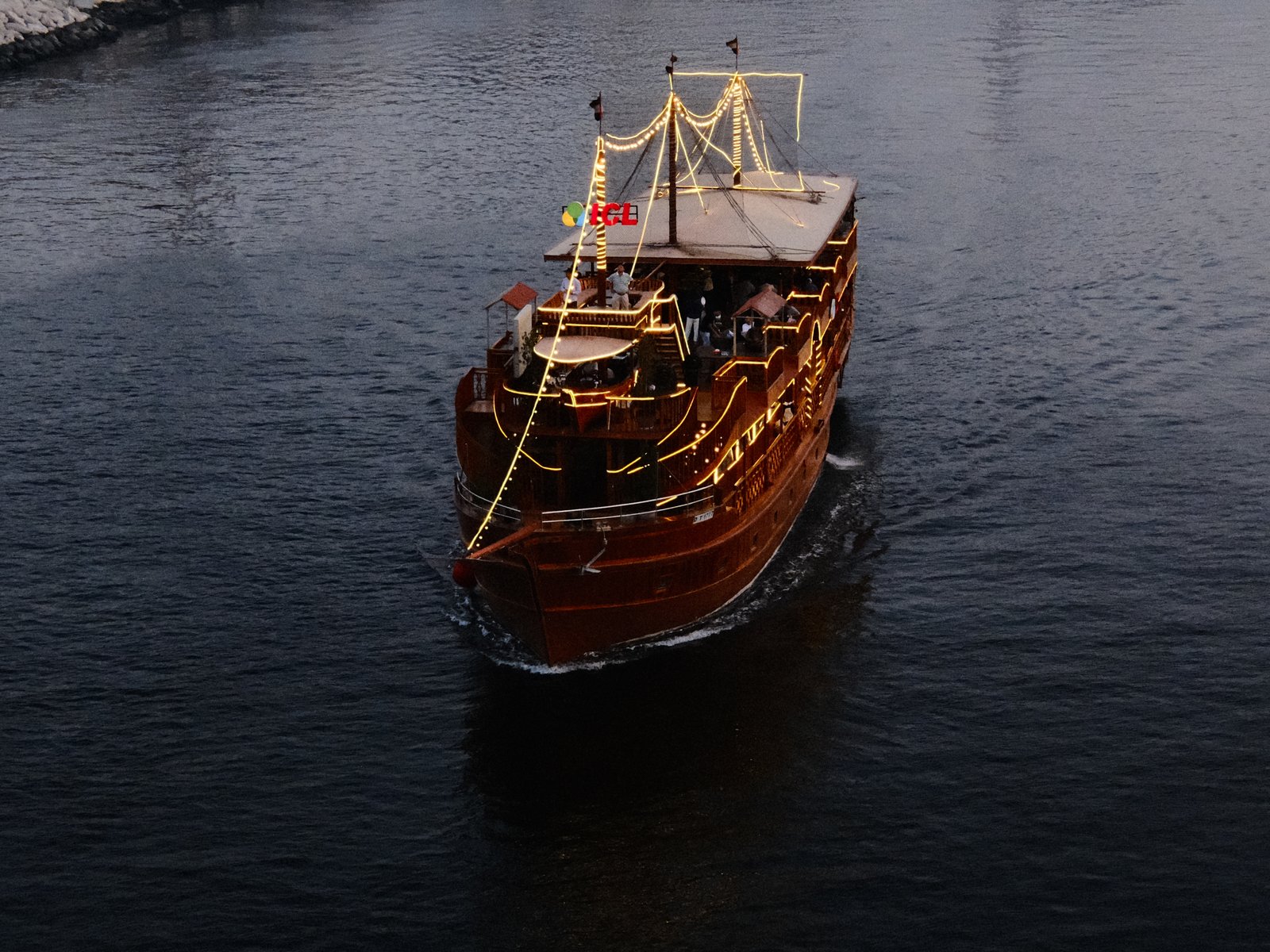 A wooden boat adorned with lights gliding through dark water, surrounded by a serene atmosphere.