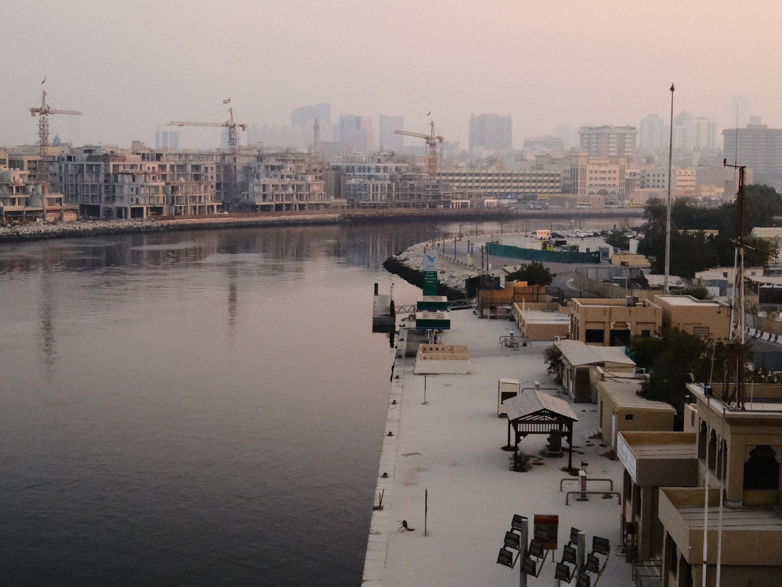 View of a river with buildings and cranes in the background during twilight.