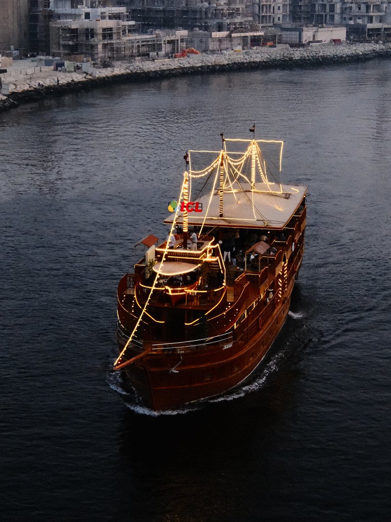 A wooden ship adorned with lights sailing on a calm river during twilight.