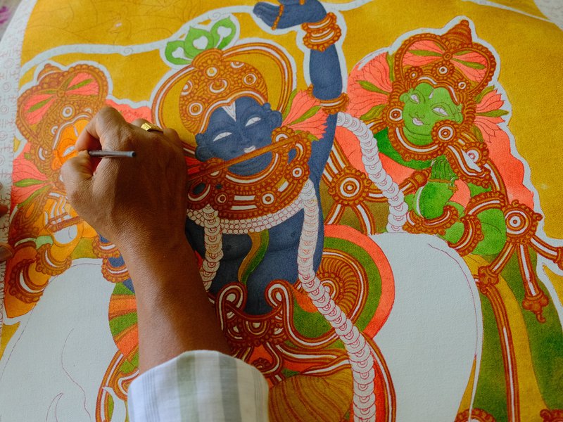 A hand painting a colorful traditional artwork featuring deities with intricate details.