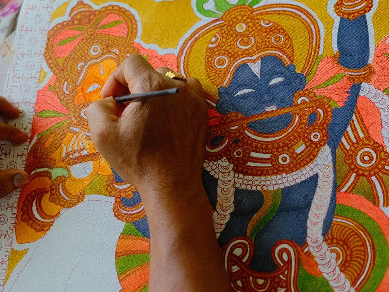 A close-up of a hand painting a colorful traditional artwork featuring a deity.