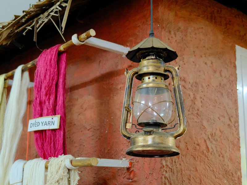 A vintage brass lantern hanging on a wall with colorful yarn and textiles nearby.