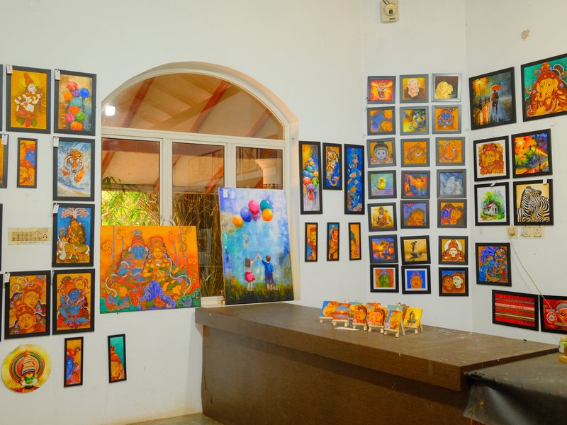 Colorful art gallery with various framed paintings on walls and a display table in front.