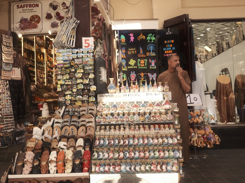 A market scene with a vendor standing beside colorful merchandise and decorative items on display.