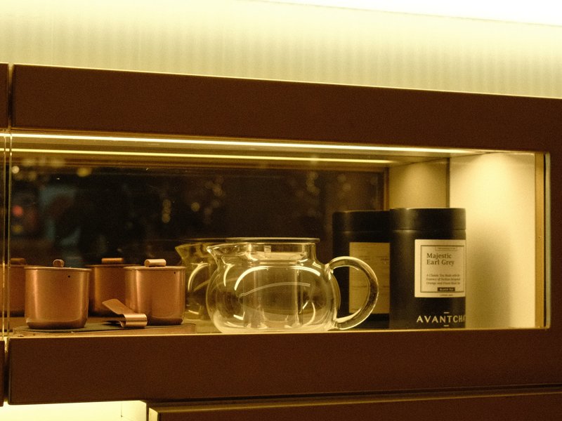 A glass teapot and tea canister displayed in a wooden cabinet with soft lighting.