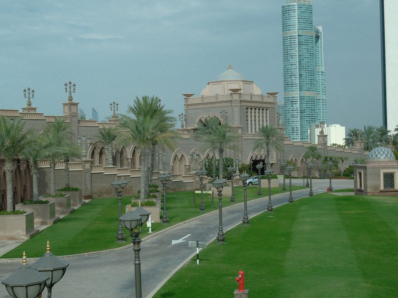 A view of a landscaped area with palm trees, a grand building, and a modern skyscraper in the background.