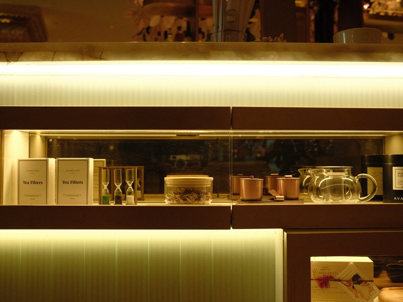 A softly lit display of various tea items and decorative containers on a shelf.