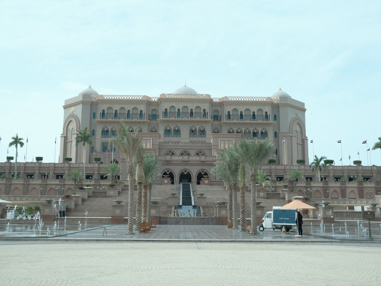 A grand architectural building with palm trees in front and a clear sky.
