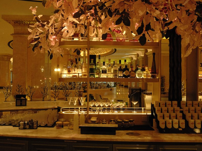 Elegant bar interior with illuminated shelves and decorative foliage.