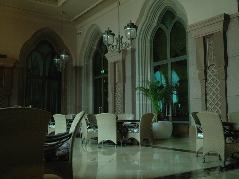 Interior of a dimly lit restaurant with elegant arches and chandeliers, featuring tables and chairs.