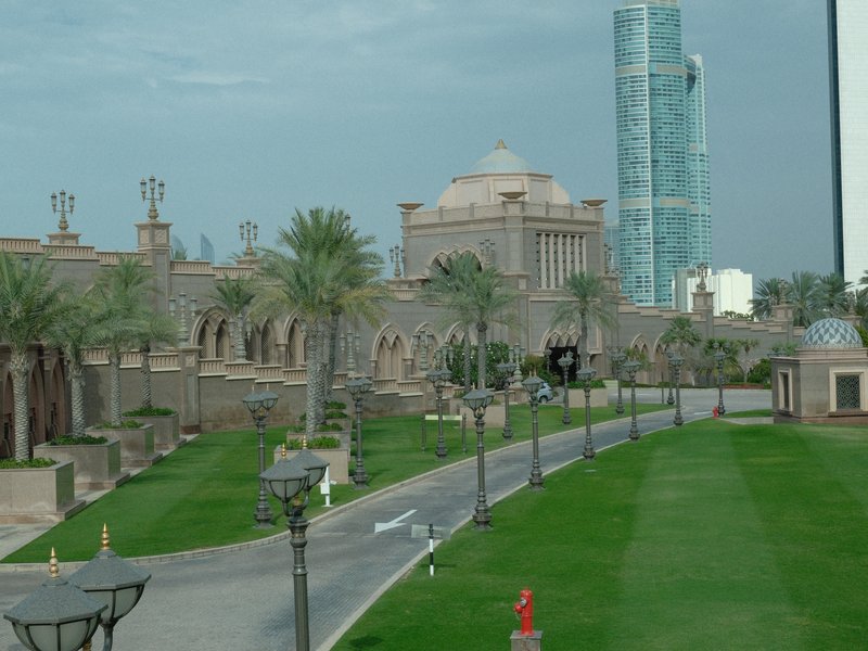 A view of a landscaped area featuring palm trees, a grand building, and modern architecture in the background.