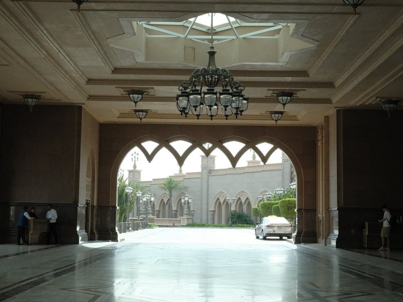 Interior view of a grand entrance with arches and a chandelier, leading to an outdoor courtyard.