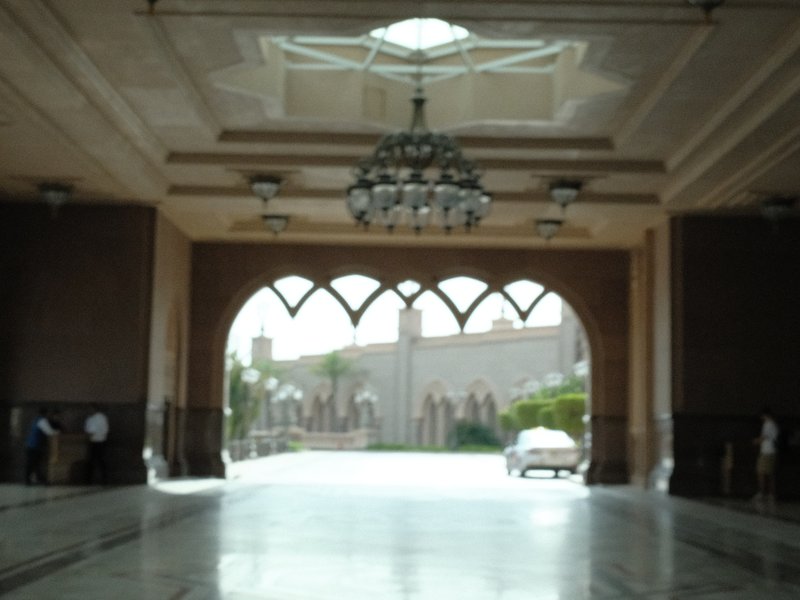 Interior view of an ornate archway with a chandelier, leading to a courtyard.