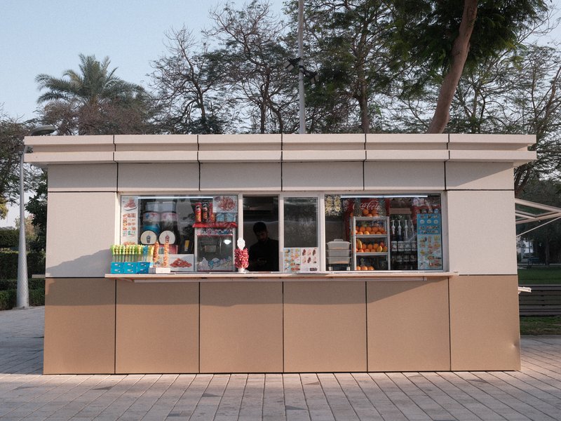 A small kiosk with various snacks and drinks displayed, surrounded by trees in a park.
