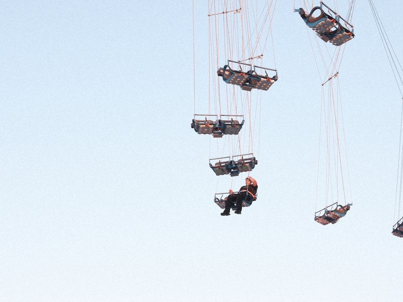A person suspended in the air, hanging from a crane with several suspended platforms above against a clear sky.