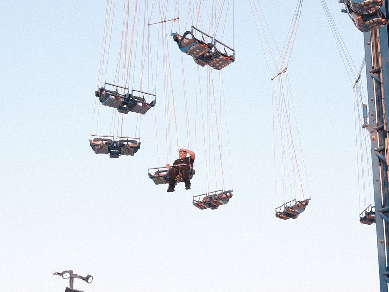 A view of several suspended swings at an amusement park against a clear blue sky.