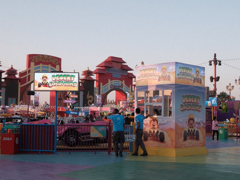 A vibrant carnival scene at dusk with colorful attractions and people interacting.