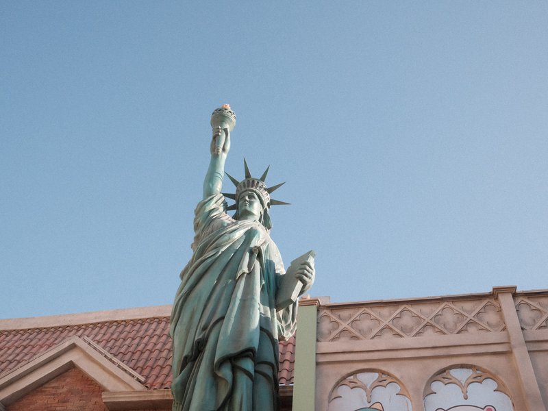 Statue of Liberty replica against a clear blue sky with a building in the background.