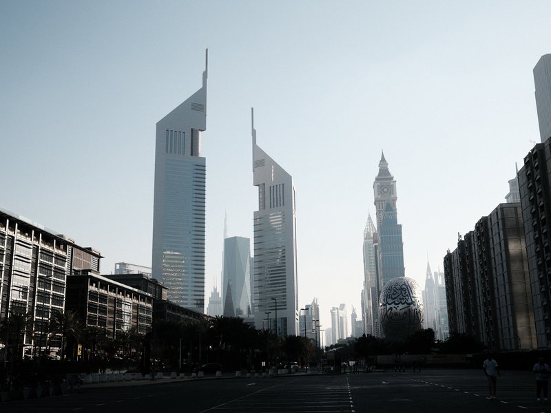 Silhouetted modern skyscrapers against a pale sky, with a wide street in the foreground.