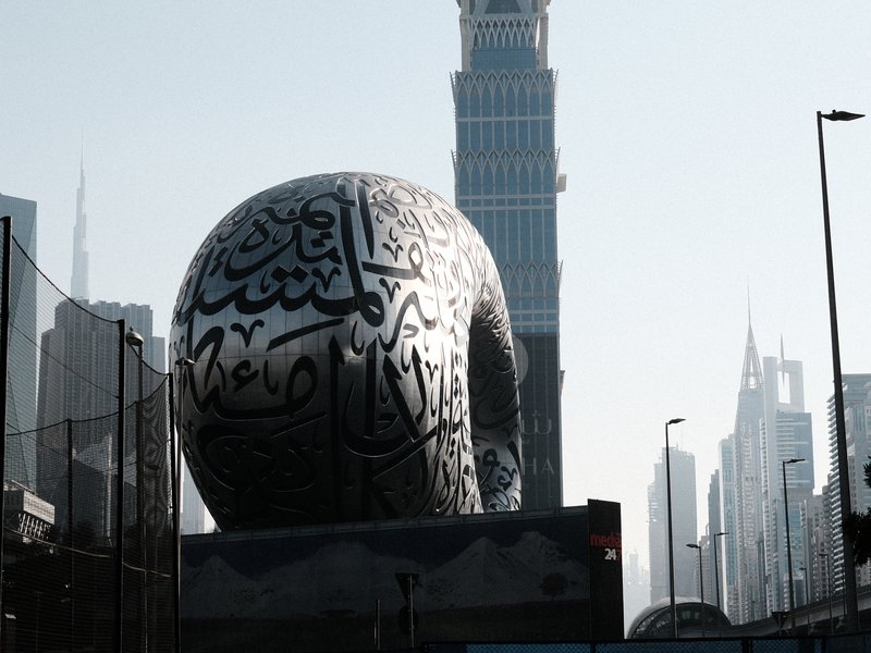A large, intricately designed spherical sculpture with Arabic calligraphy in an urban setting with skyscrapers.