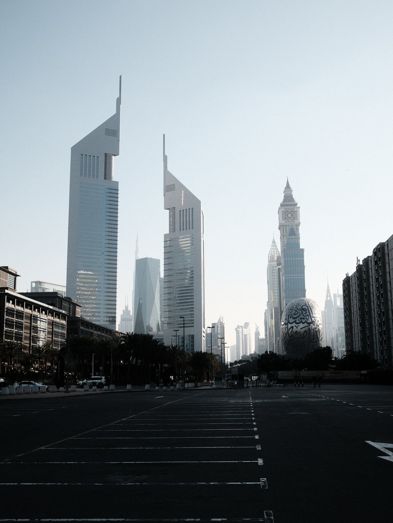 Silhouette of modern skyscrapers against a pale sky, with an empty street in the foreground.