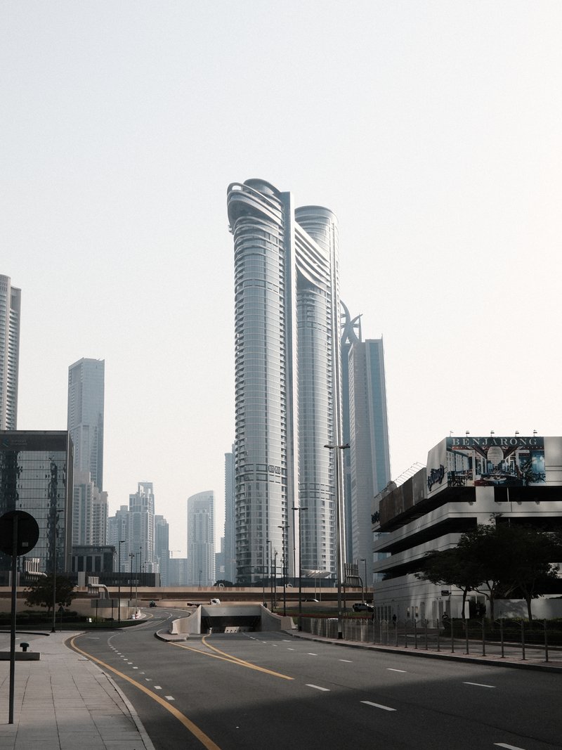 Two modern skyscrapers rise above a deserted urban street under a clear sky.