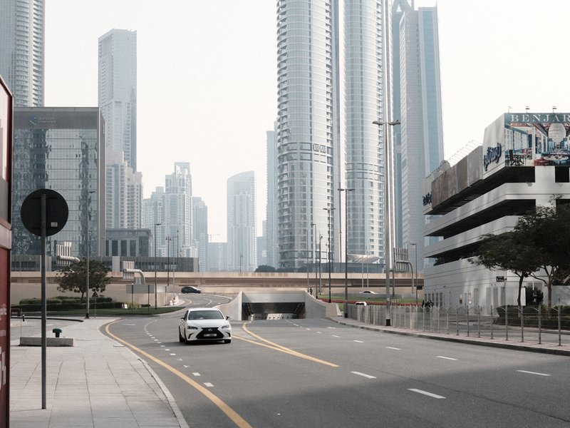 A quiet urban street with a white car, surrounded by tall skyscrapers and modern architecture.