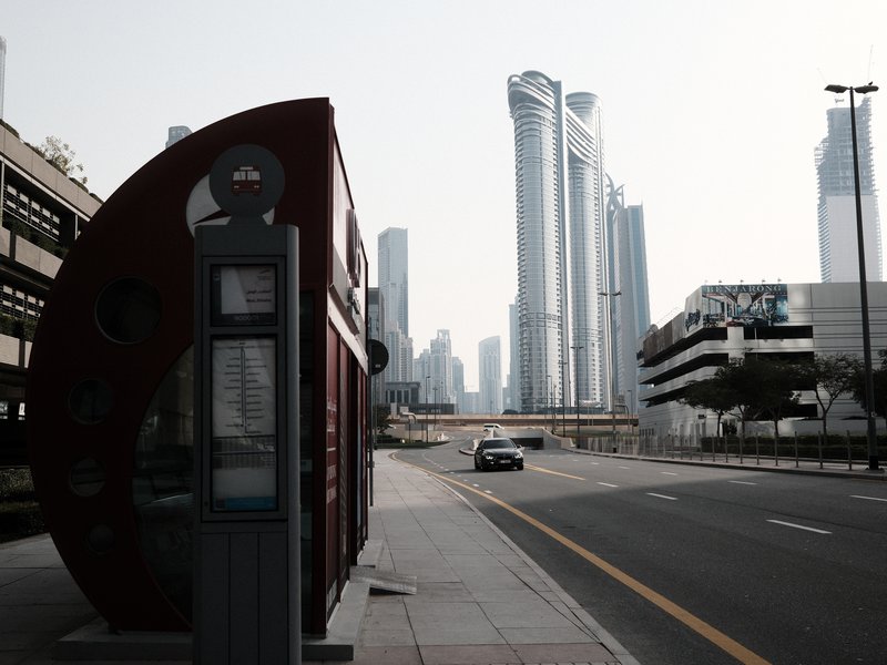 A modern urban scene featuring a bus stop and skyscrapers in the background under a hazy sky.