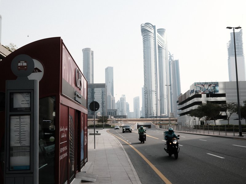 Urban scene with tall skyscrapers, a bus stop, and motorcycles on a road.