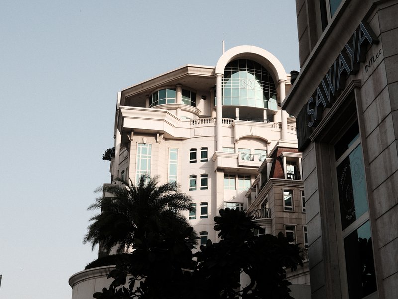 A modern building with a curved roof and large windows, surrounded by palm trees and urban architecture.