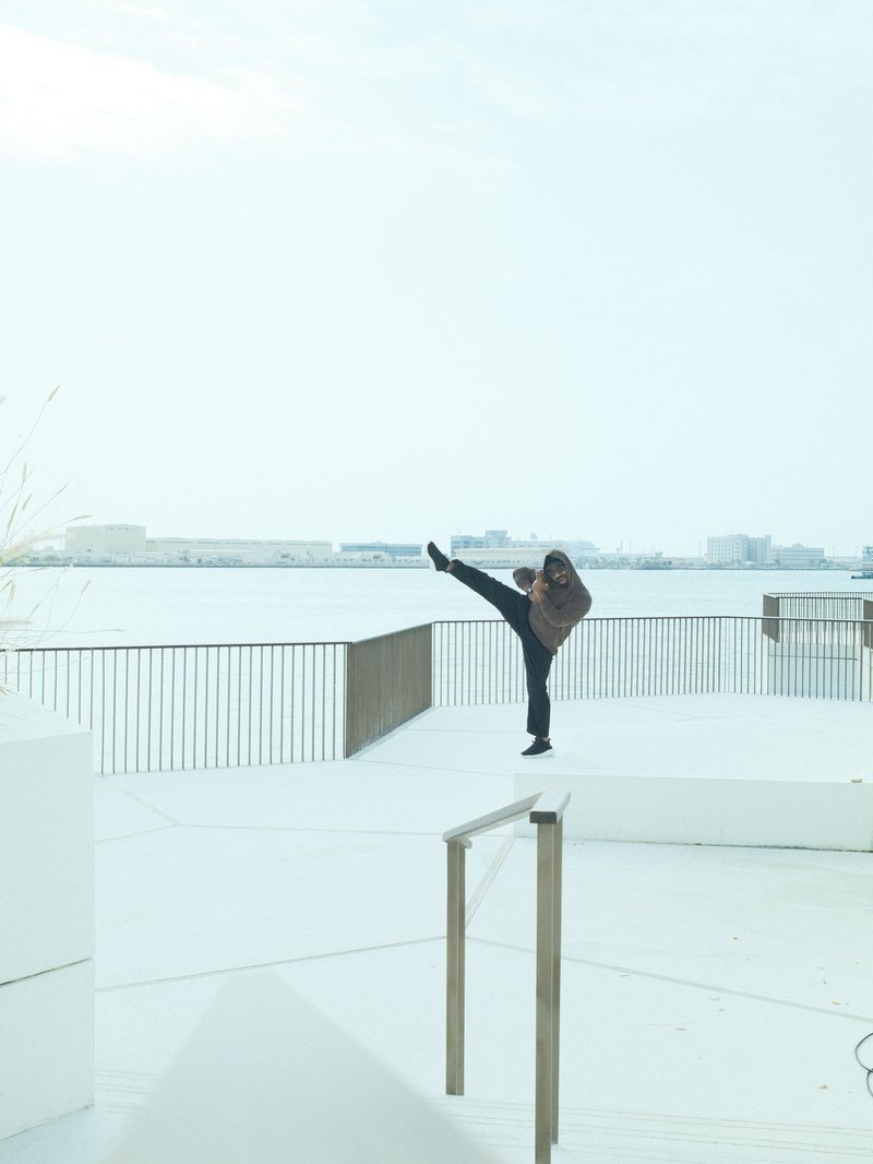 A person performing a high kick on a snowy outdoor platform with a view of a body of water.