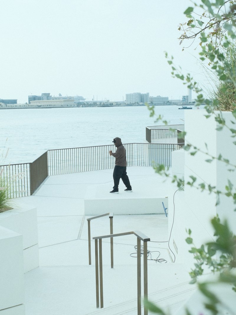 A person walking on a white terrace by the water, with a city skyline in the background.