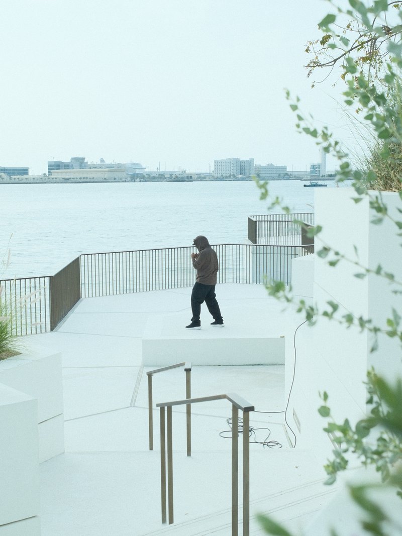 A person walking on a white terrace by the water, with a city skyline in the background.
