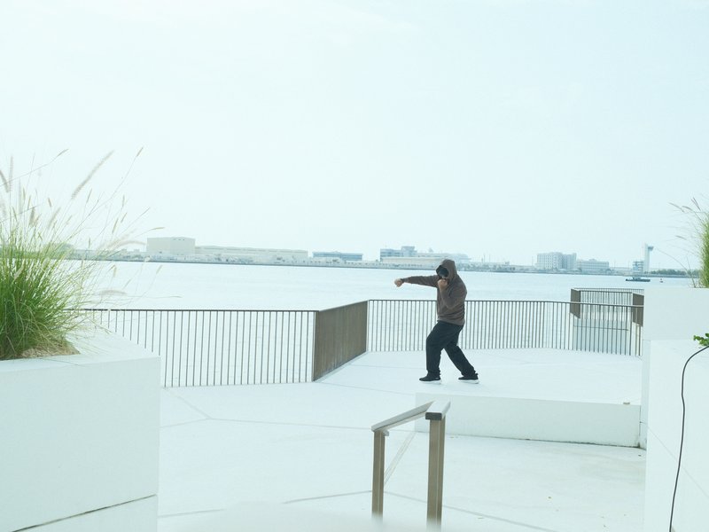 A person performing a dance move on a white deck by the water, with a hazy skyline in the background.