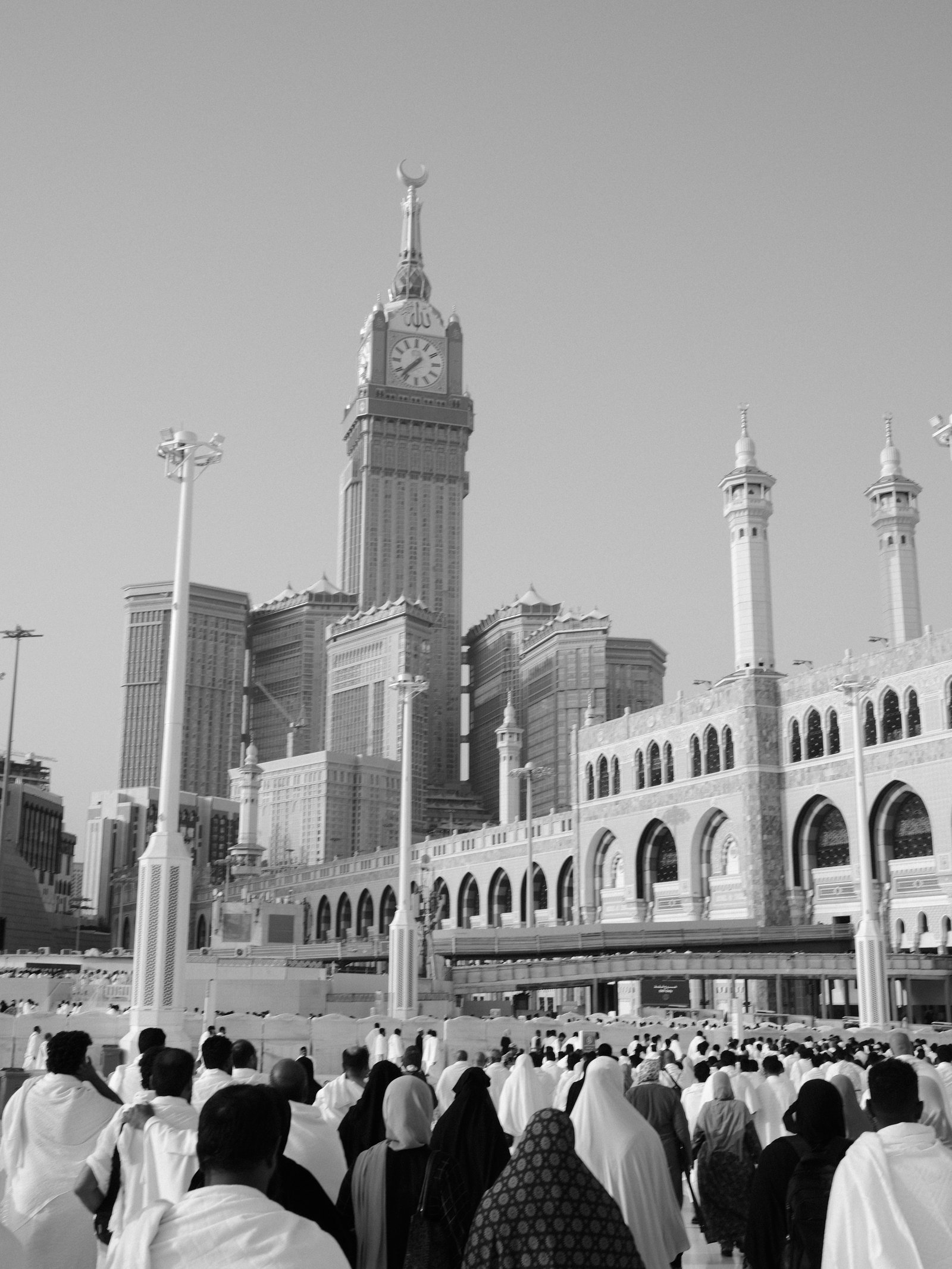 Crowd of people in white garments walking towards a large building in a cityscape.