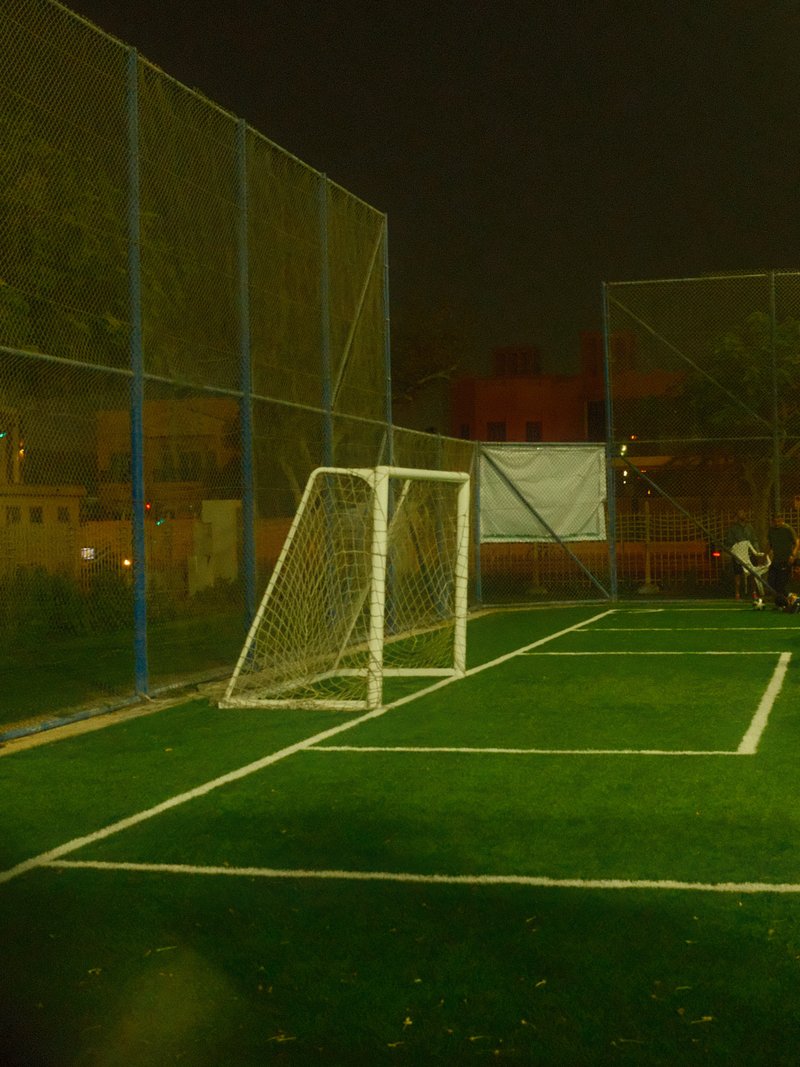 A dimly lit soccer field at night with a goalpost and surrounding fencing.