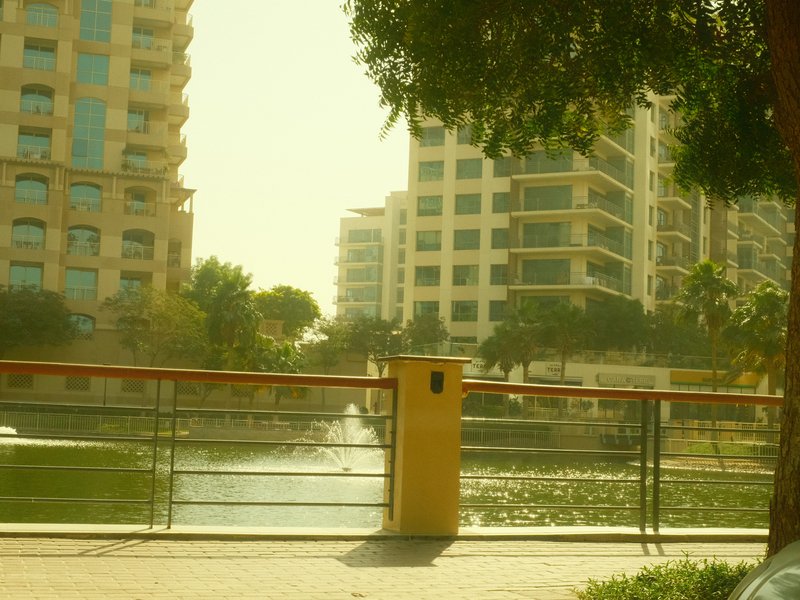 A serene view of a canal lined with modern buildings under a hazy yellow light.