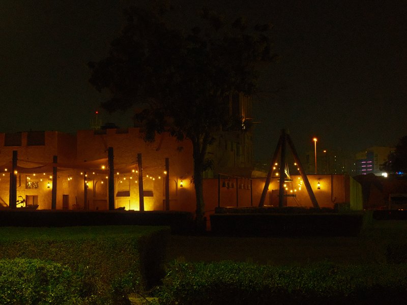Dimly lit outdoor area with a playground and warm lights against a dark night sky.