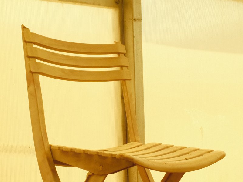 A simple wooden chair against a soft yellow backdrop.